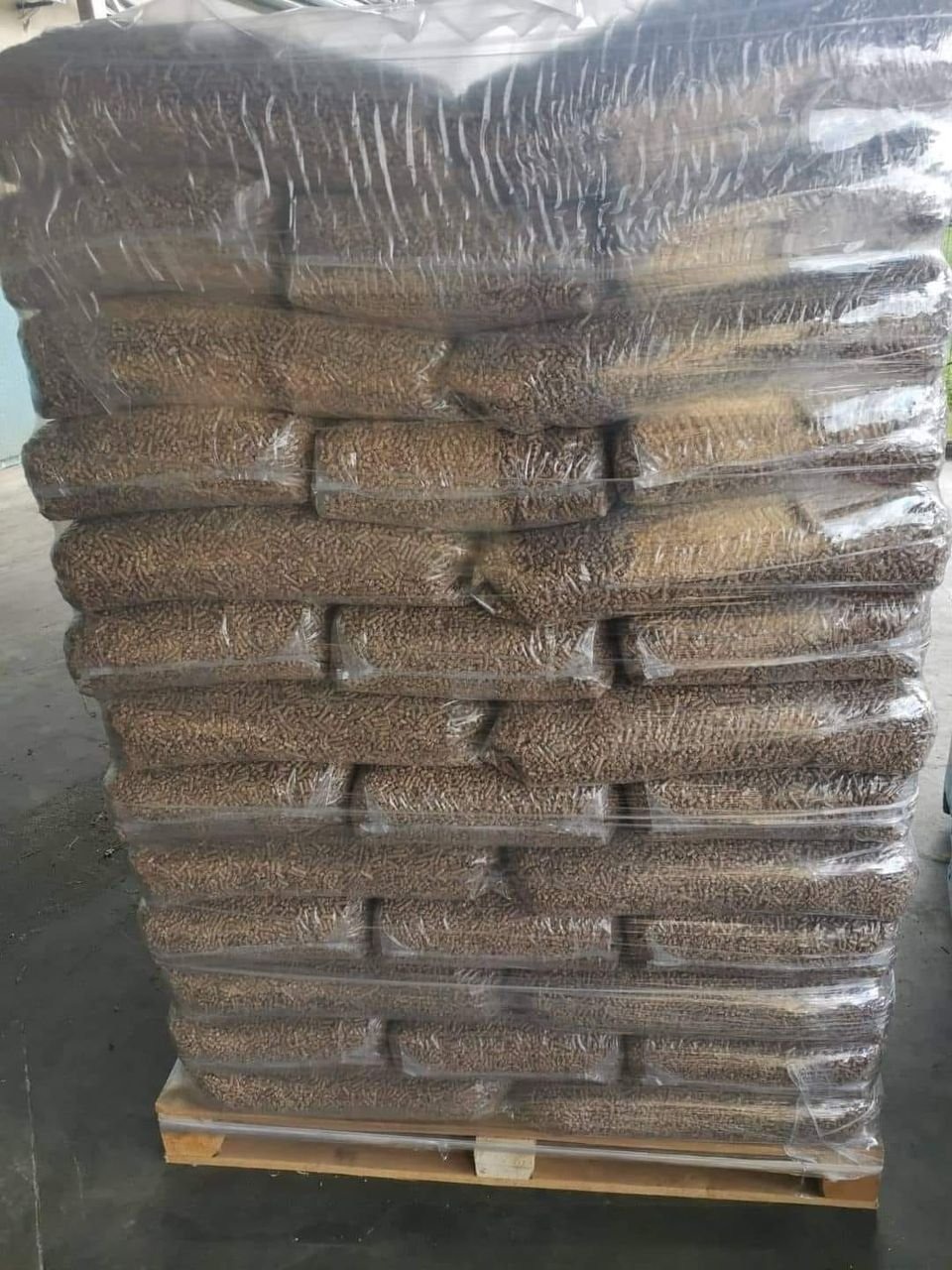 Ułożone w stos worki z pelletem na drewnianej palecie, owinięte przezroczystą folią stretch.