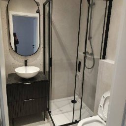 REMONTY I WYKOŃCZENIA KRZYSZTOF PAZIEWSKI - Nowoczesna łazienka z czarną kabiną prysznicową, umywalką na szafce z ryflowanym frontem i owalnym lustrem z podświetleniem. Minimalistyczny design i jasne wykończenie ścian.