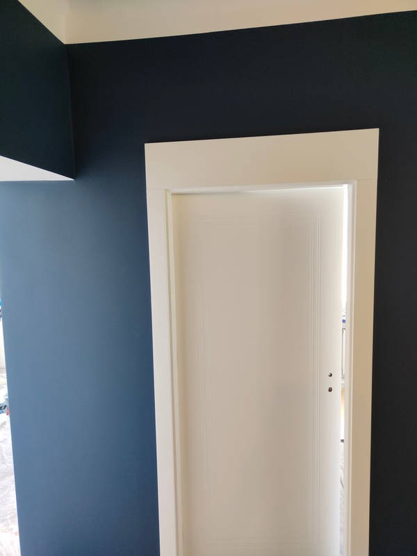 Wnętrze po malowaniu: granatowe ściany, białe listwy sufitowe i ościeżnica z zamontowanymi białymi drzwiami. Widok na pomalowane pomieszczenie.