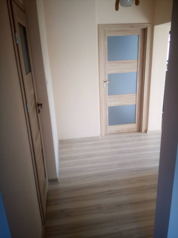 Jasne, drewniane drzwi z trzema szybami w wyremontowanym korytarzu z panelami podłogowymi. Widok z perspektywy wejścia do pomieszczenia.