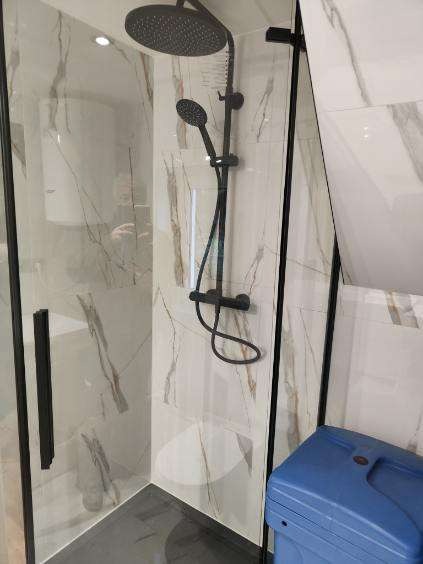 Nowoczesna kabina prysznicowa z czarną armaturą i marmurowymi płytkami. Uwagę zwraca niebieski pojemnik z boku i czarny brodzik.