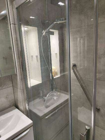 Nowoczesna kabina prysznicowa z szarą glazurą, umywalką i półkami wnękowymi. Minimalistyczny design, widok z boku.