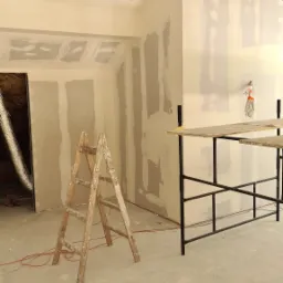 Poddasze w trakcie wykańczania płytami kartonowo-gipsowymi, widoczne szpachlowane łączenia, drabina drewniana i rusztowanie metalowe.