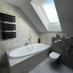 Remontada - Jasna łazienka na poddaszu z owalną wanną, grzejnikiem drabinkowym, toaletą podwieszaną i oknem dachowym w skosie.
