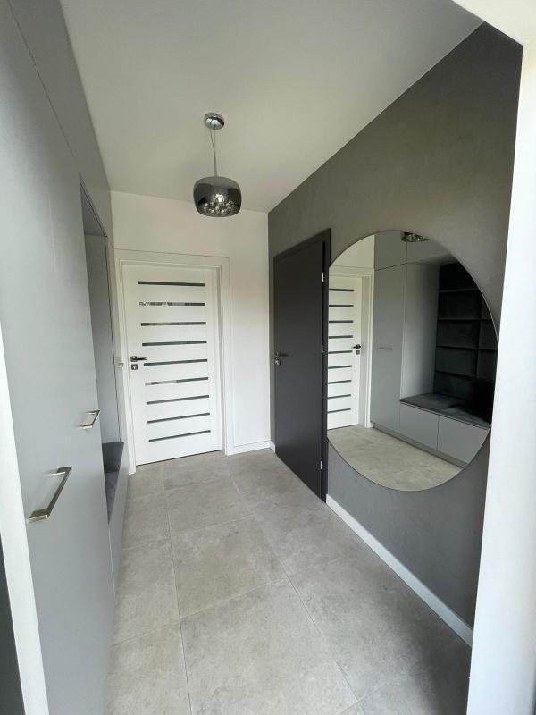 Nowoczesny przedpokój w szarościach z okrągłym lustrem, minimalistyczną lampą wiszącą, i drzwiami z poziomymi przeszkleniami, wykończony płytkami podłogowymi w odcieniach szarości.