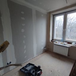 SkillWorks Michał Rzeszutek - Ściana z płyt karton gipsowych w trakcie szpachlowania, widoczne narzędzia i skrzynka narzędziowa w pomieszczeniu w Tuszowie Narodowym, okno z widokiem na drzewa.