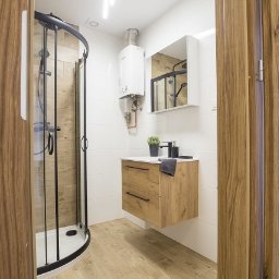 SkillWorks Michał Rzeszutek - Nowoczesna łazienka z kabiną prysznicową z czarnymi profilami, wiszącą szafką z drewnianym fornirem, białymi płytkami ściennymi i grzejnikiem gazowym.