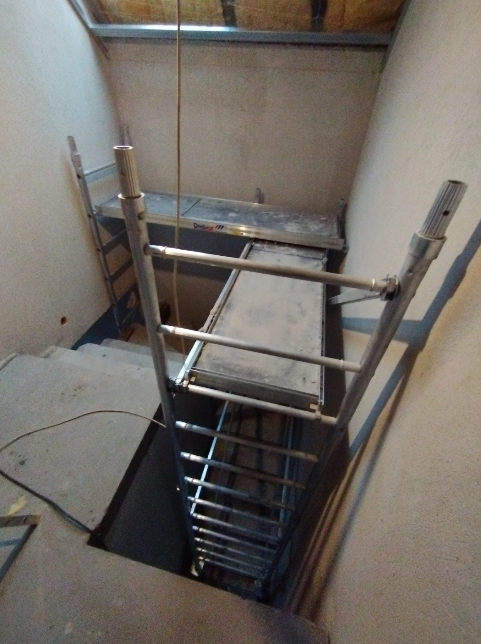 Metalowe rusztowanie w wąskim korytarzu na schodach, przygotowane do prac wykończeniowych, widoczne ślady po pracach na ścianach i suficie.