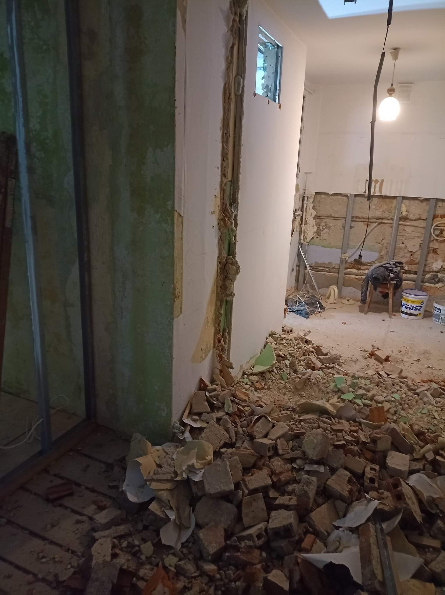 Wnętrze w trakcie rozbiórki, z widocznymi fragmentami gruzu, odsłoniętymi instalacjami i elementami konstrukcyjnymi ścian, z puszką farby 'Finisz' w tle.