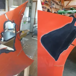 Pomarańczowy element karoserii z widocznym uszkodzeniem i fragmentem procesu naprawy, z czarnym wypełnieniem ubytku.