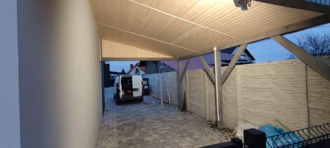 Zadaszenie tarasu z drewnianą konstrukcją i podbitką z paneli, widoczny samochód dostawczy i drabina oparta o betonowy płot.