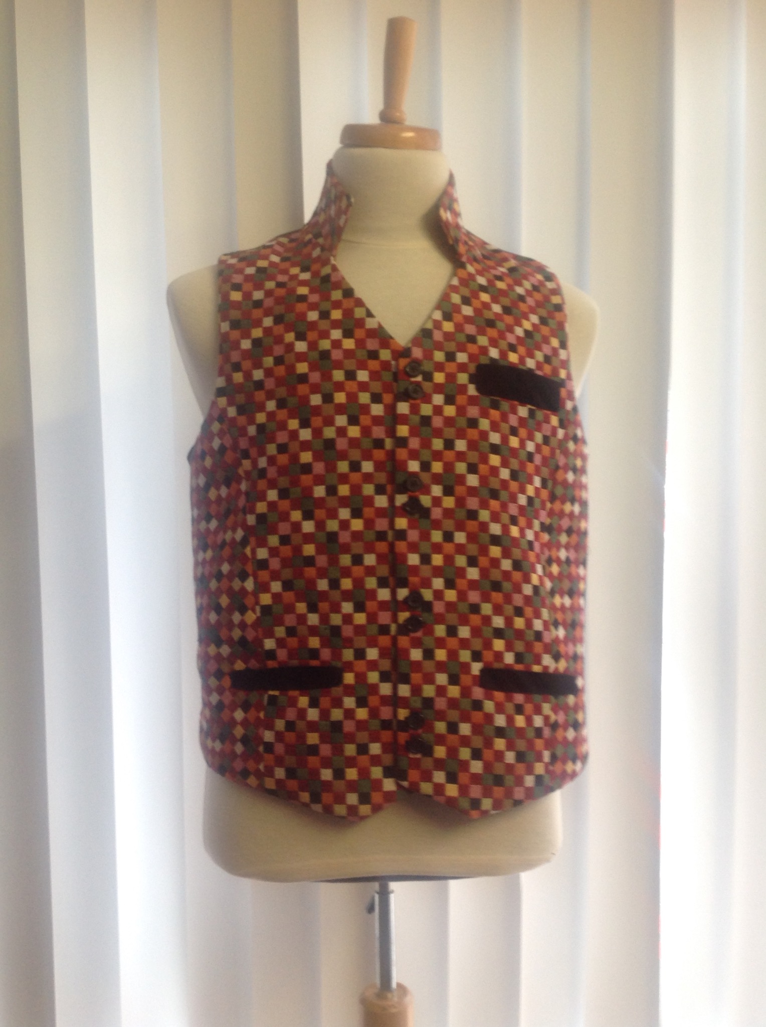 Kamizelka męska w drobny wzór w kratkę, prezentowana na manekinie krawieckim z drewnianą podstawą, na tle białych zasłon.