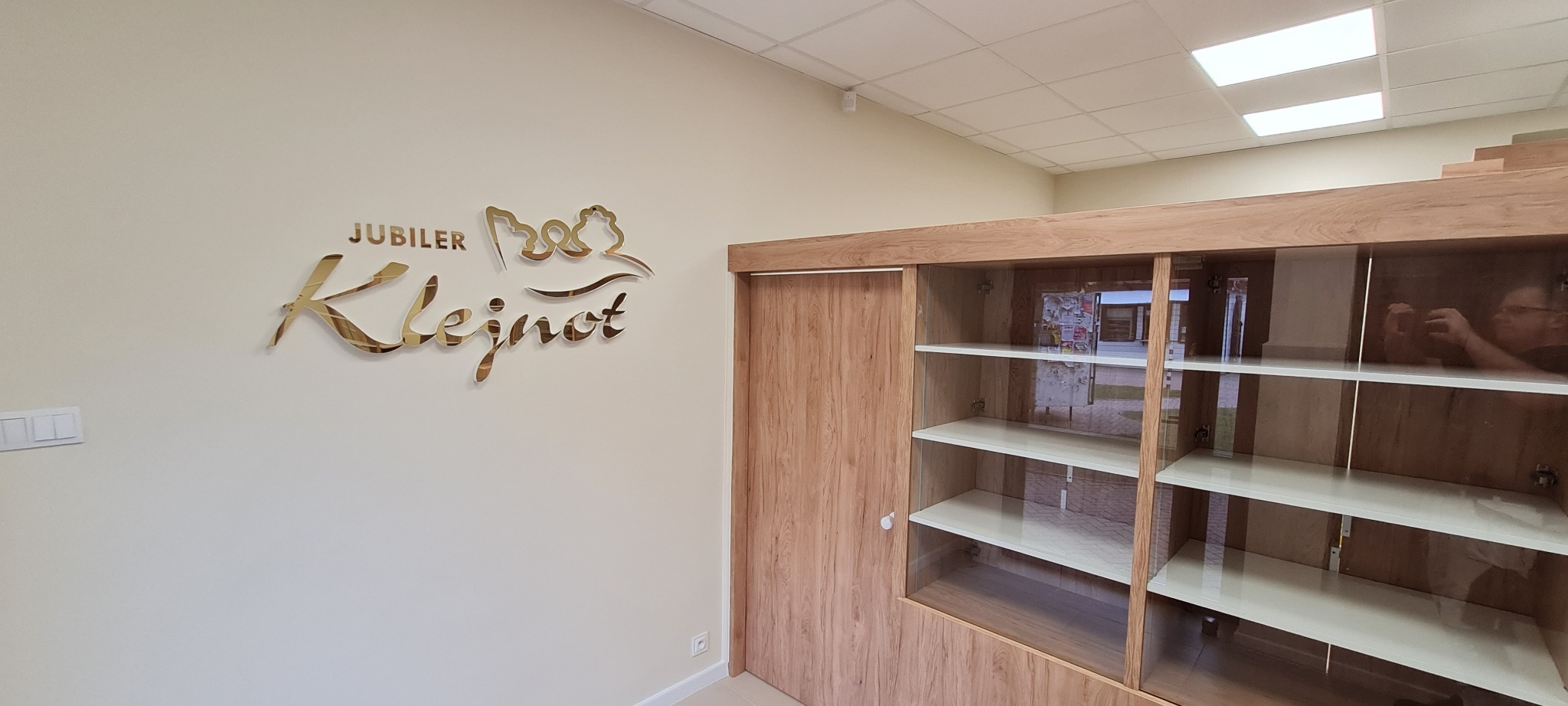 Wnętrze salonu jubilerskiego Klejnot po remoncie: złoty napis firmowy na ścianie, zabudowa meblowa z drewnopodobnymi frontami i szklanymi witrynami.