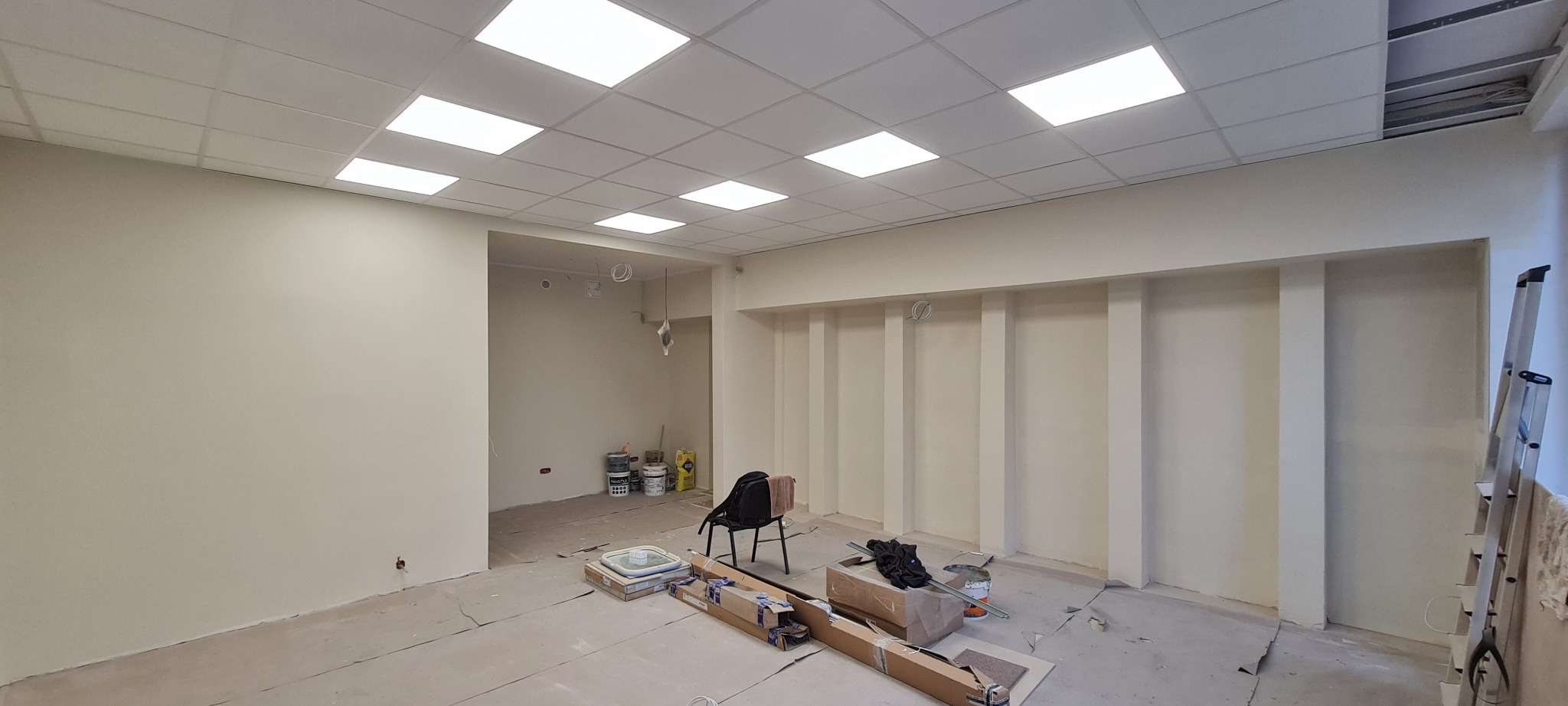 Wnętrze salonu jubilerskiego w trakcie remontu, świeżo pomalowane ściany w odcieniach beżu, widoczne puszki z farbą, rozłożone kartony i drabina.