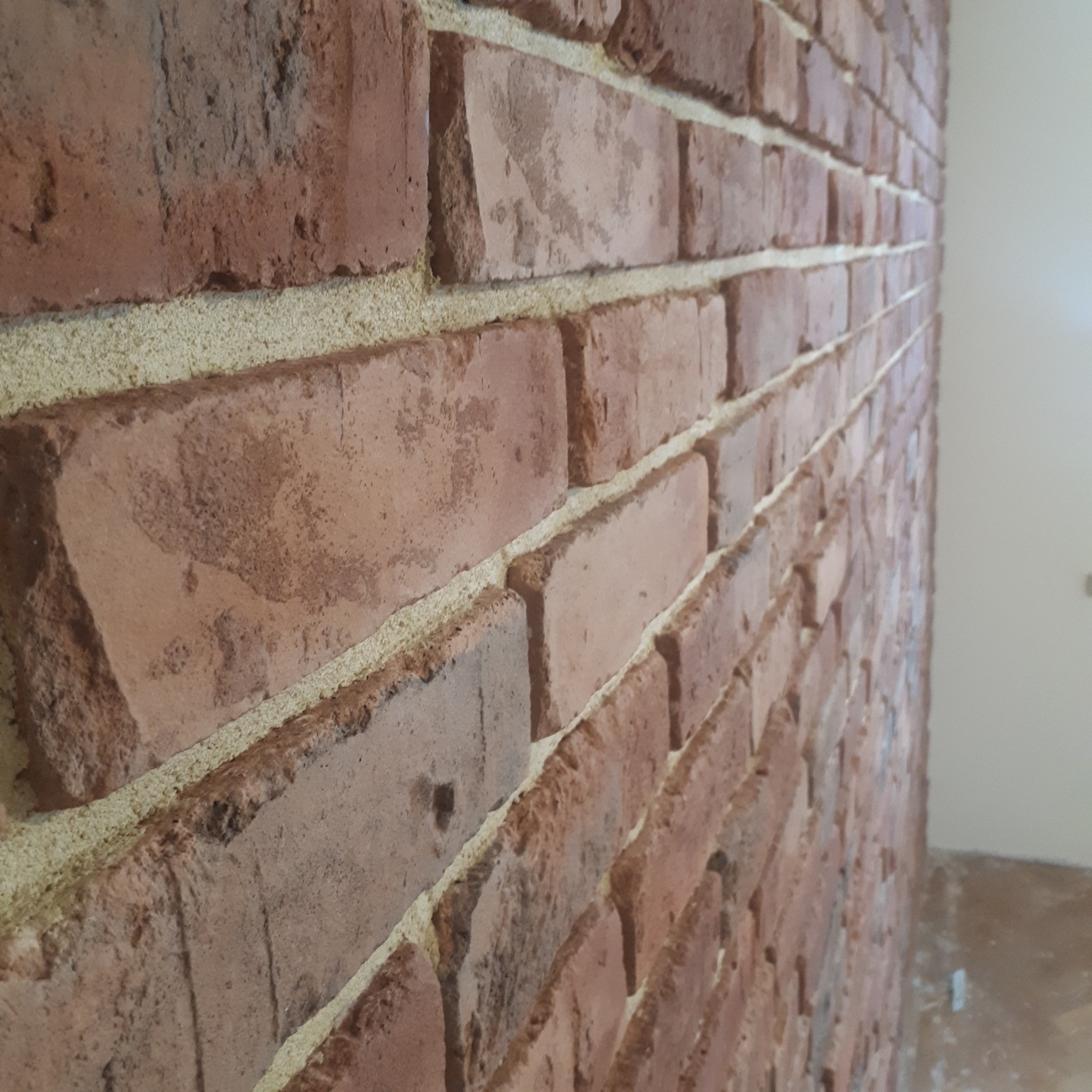 Ściana wykończona czerwoną cegłą ciętą, z widoczną strukturą i jasną spoiną, sfotografowana pod kątem z bliska.