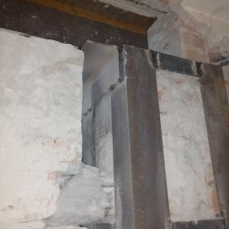 Paweł Brodowicz - Wzmocnienie otworu w ścianie za pomocą stalowych belek, widoczne fragmenty cegieł i zaprawy, surowy stan przed dalszymi pracami.