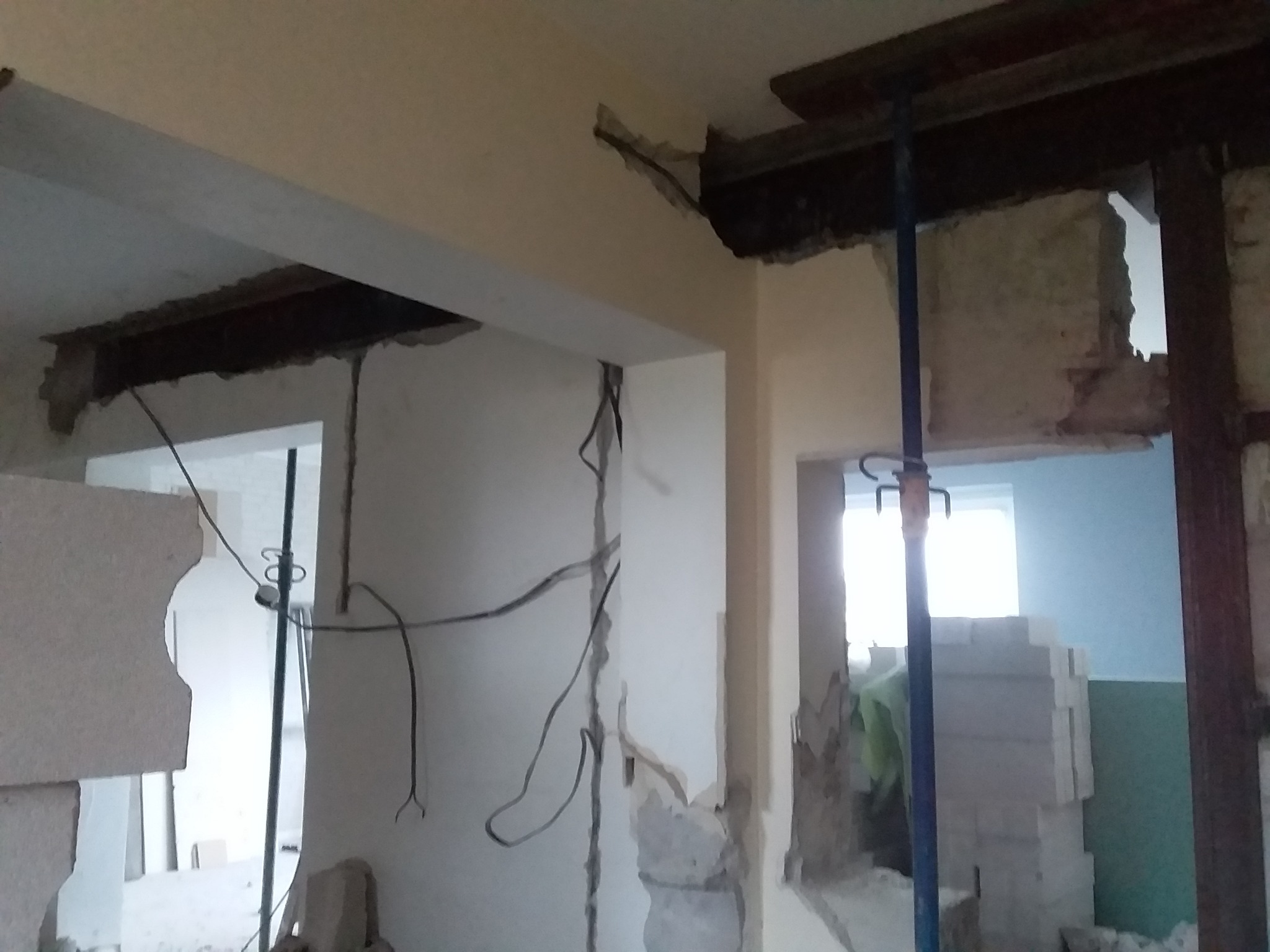 Demontaż ściany działowej z odsłoniętymi przewodami elektrycznymi i wspornikami stropowymi, widoczne gruzy i elementy konstrukcyjne w trakcie prac remontowych.