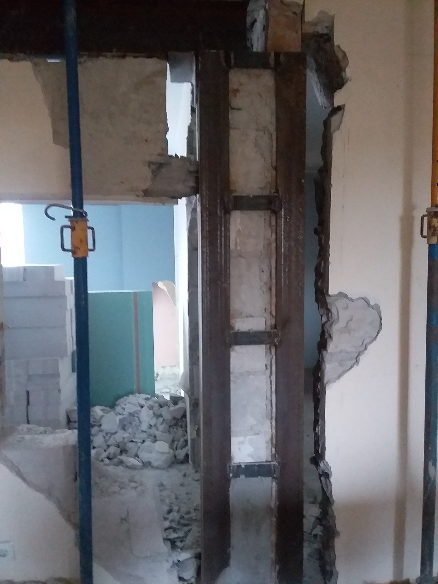 Wzmocnienie otworu w ścianie z widocznymi elementami stalowymi i gruzem, podpora stropu widoczna w tle.