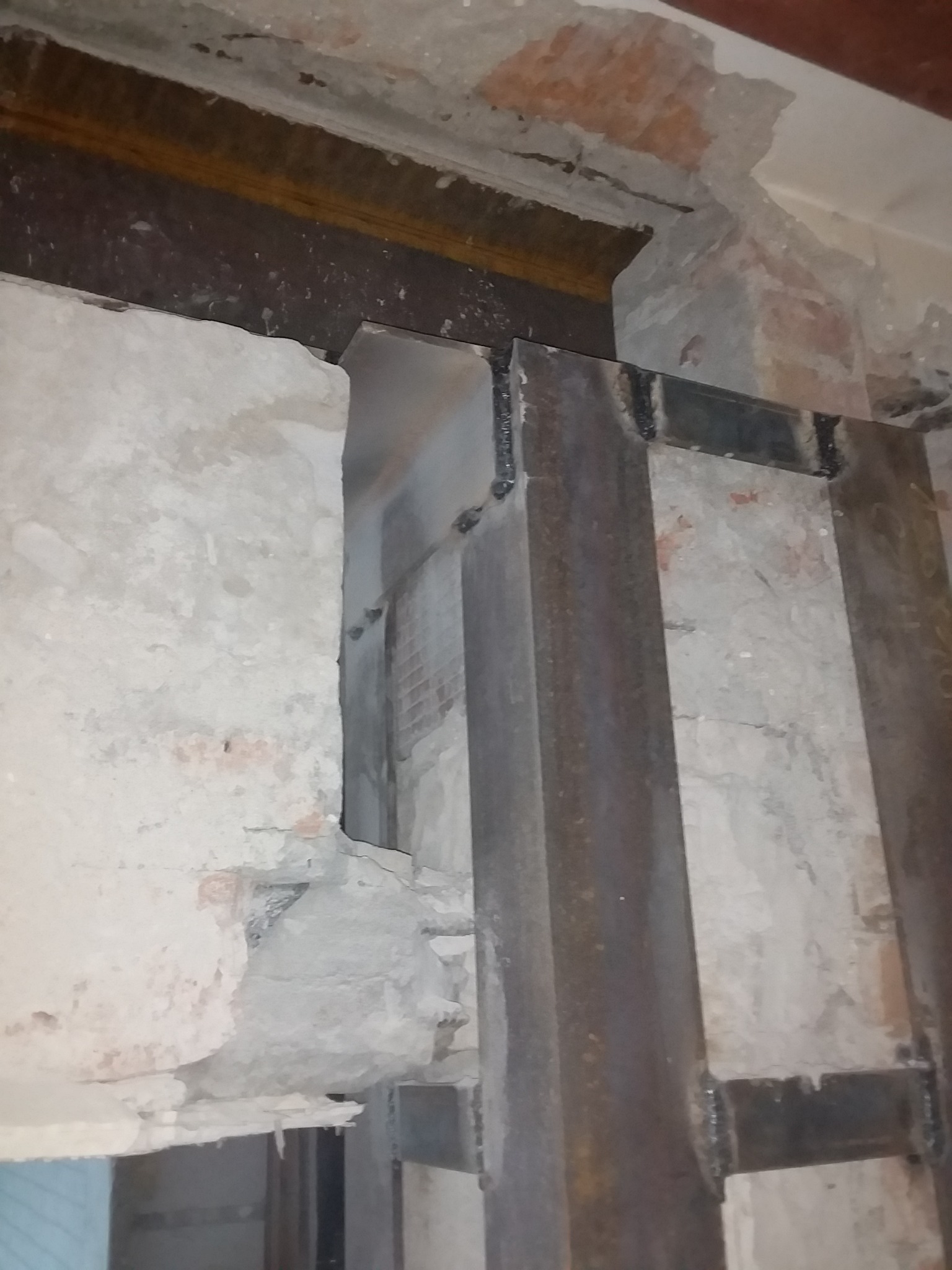 Wzmocnienie otworu w ścianie za pomocą stalowych belek, widoczne fragmenty cegieł i zaprawy, surowy stan przed dalszymi pracami.