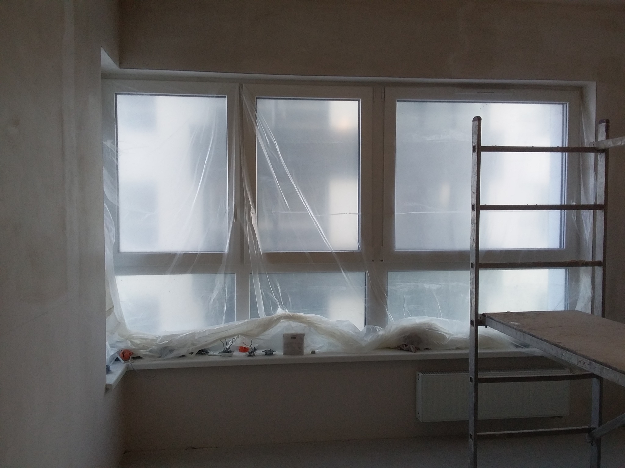 Przygotowanie do malowania: Okna zabezpieczone folią malarską, widoczny fragment rusztowania, ściany po wstępnym szpachlowaniu.