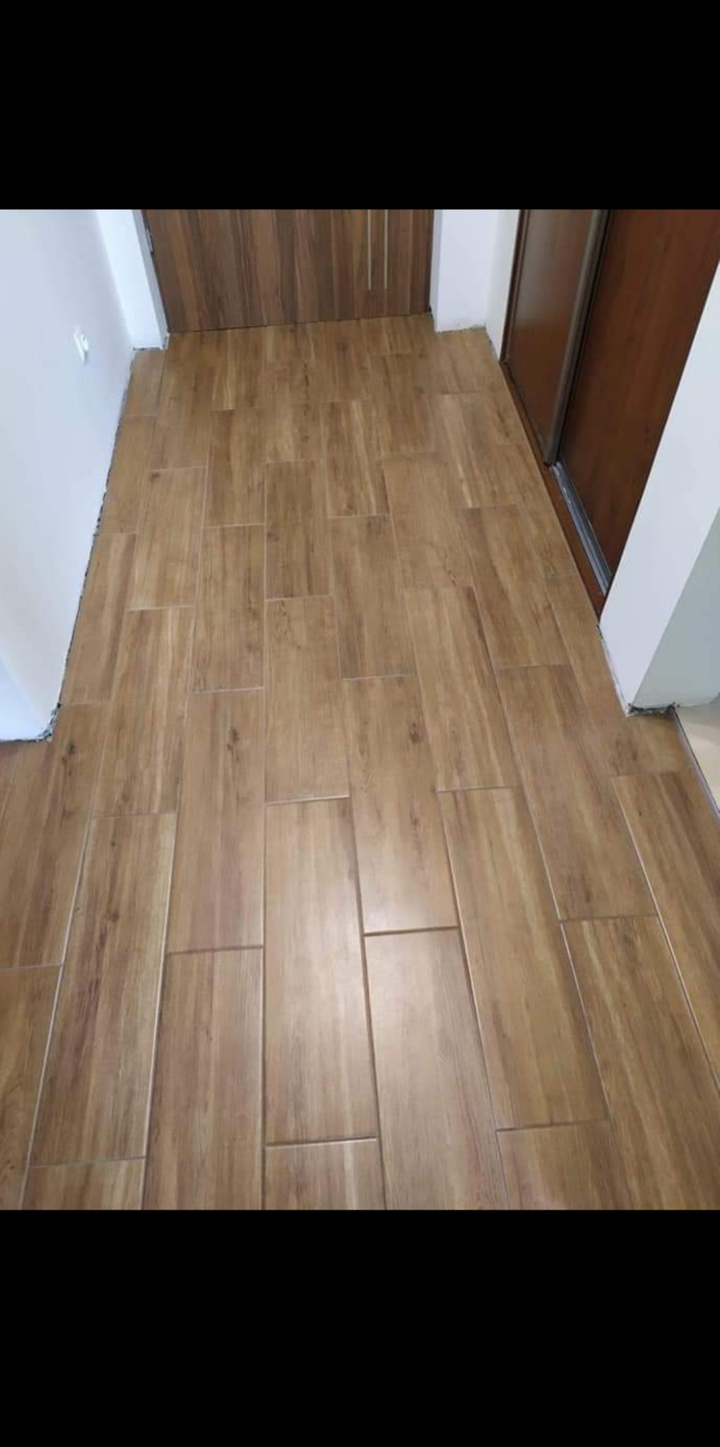 Ułożone podłużne panele podłogowe imitujące drewno w korytarzu, widoczne niedociągnięcia przy ścianach i ościeżnicach drzwi.