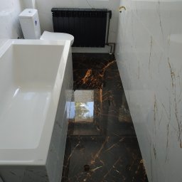 Sna Bud - Nowoczesna łazienka z białą wanną KOLO, toaletą i czarnym grzejnikiem, wykończona marmurowymi płytkami w odcieniach bieli i brązu.