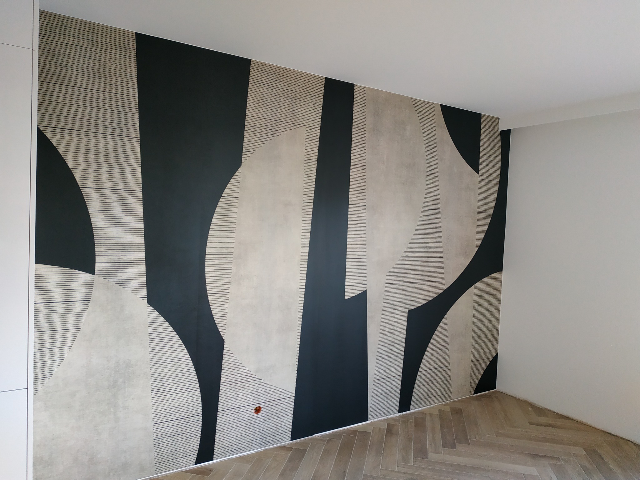 Ściana pokryta tapetą z geometrycznym wzorem w odcieniach szarości i czerni, ułożona na ścianie w nowocześnie wykończonym wnętrzu z parkietem w jodełkę.