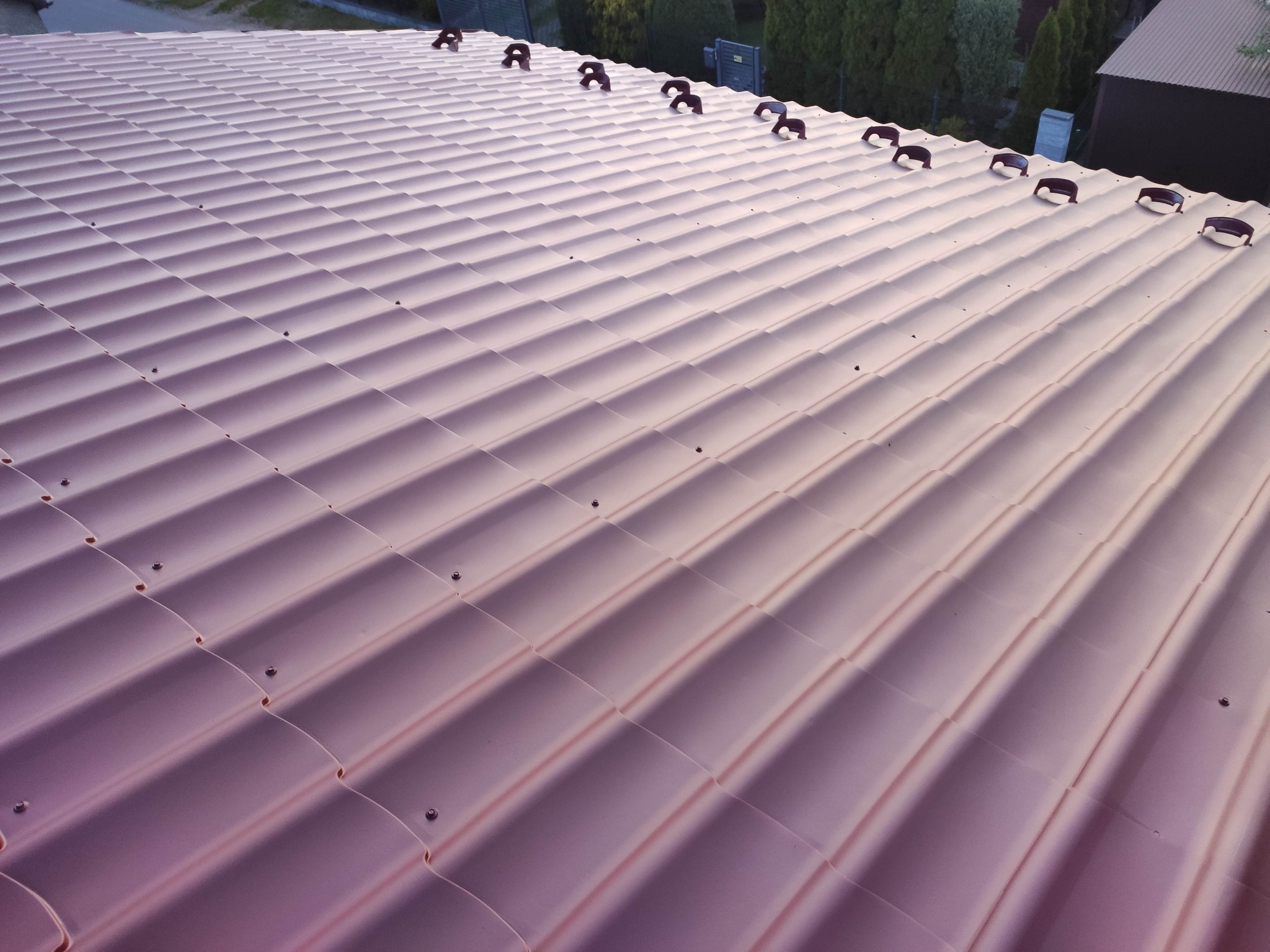 Nowy, lśniący dach z blachodachówki w odcieniach różu, zabezpieczony brązowymi śniegołapami, widok z góry.