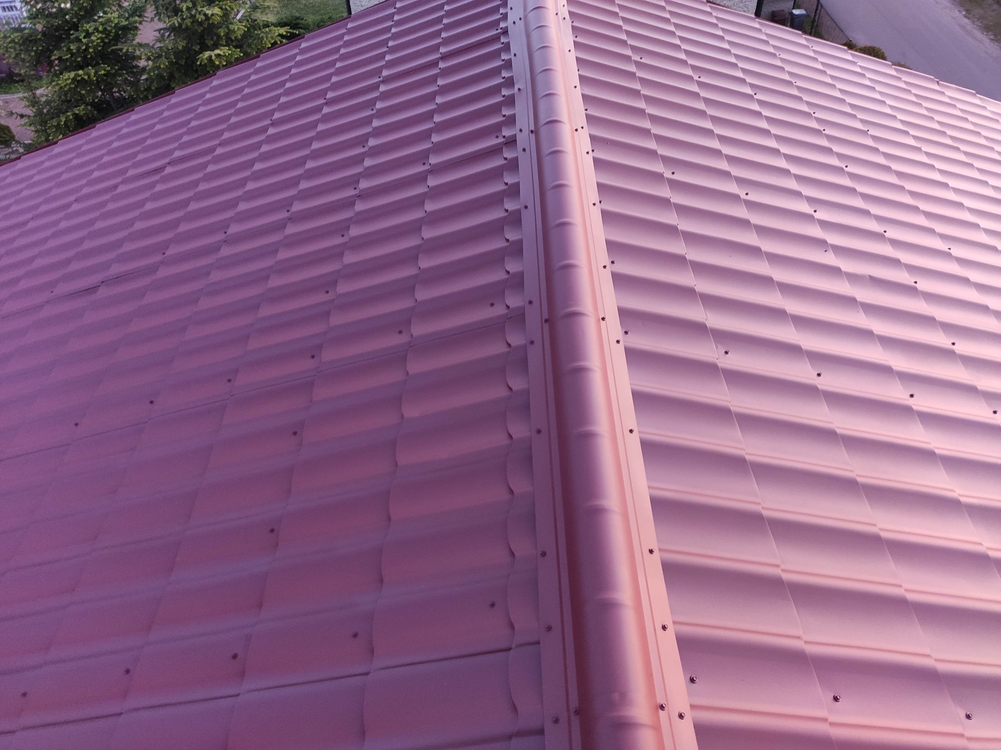 Nowy, metalowy dach w kolorze miedzianego różu z widocznym łączeniem paneli i elementami mocującymi, sfotografowany pod kątem.