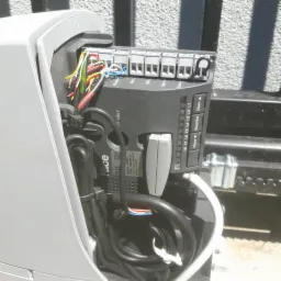 Otwarta obudowa sterownika bramy automatycznej Nice z widocznymi przewodami, listwą zaciskową i modułem sterującym, z naklejką informacyjną o modelu i kraju produkcji.