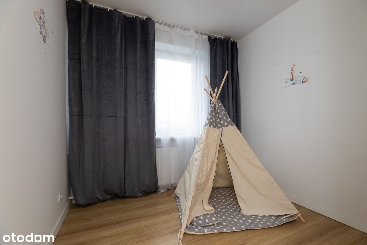 Pokój dziecięcy z beżowym tipi z szarą górą w białe gwiazdki, szare welurowe zasłony i naklejki z motywami zwierzęcymi na białych ścianach, na podłodze panele w kolorze drewna.