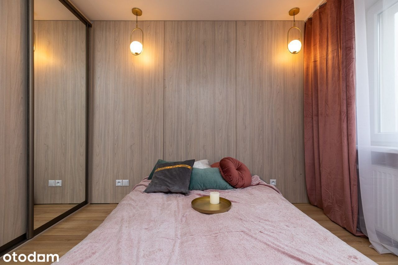 Nowoczesna sypialnia z drewnianą zabudową, okrągłymi lampami wiszącymi, różową narzutą na łóżku i zasłonami w odcieniu dusty rose, minimalistyczny design.