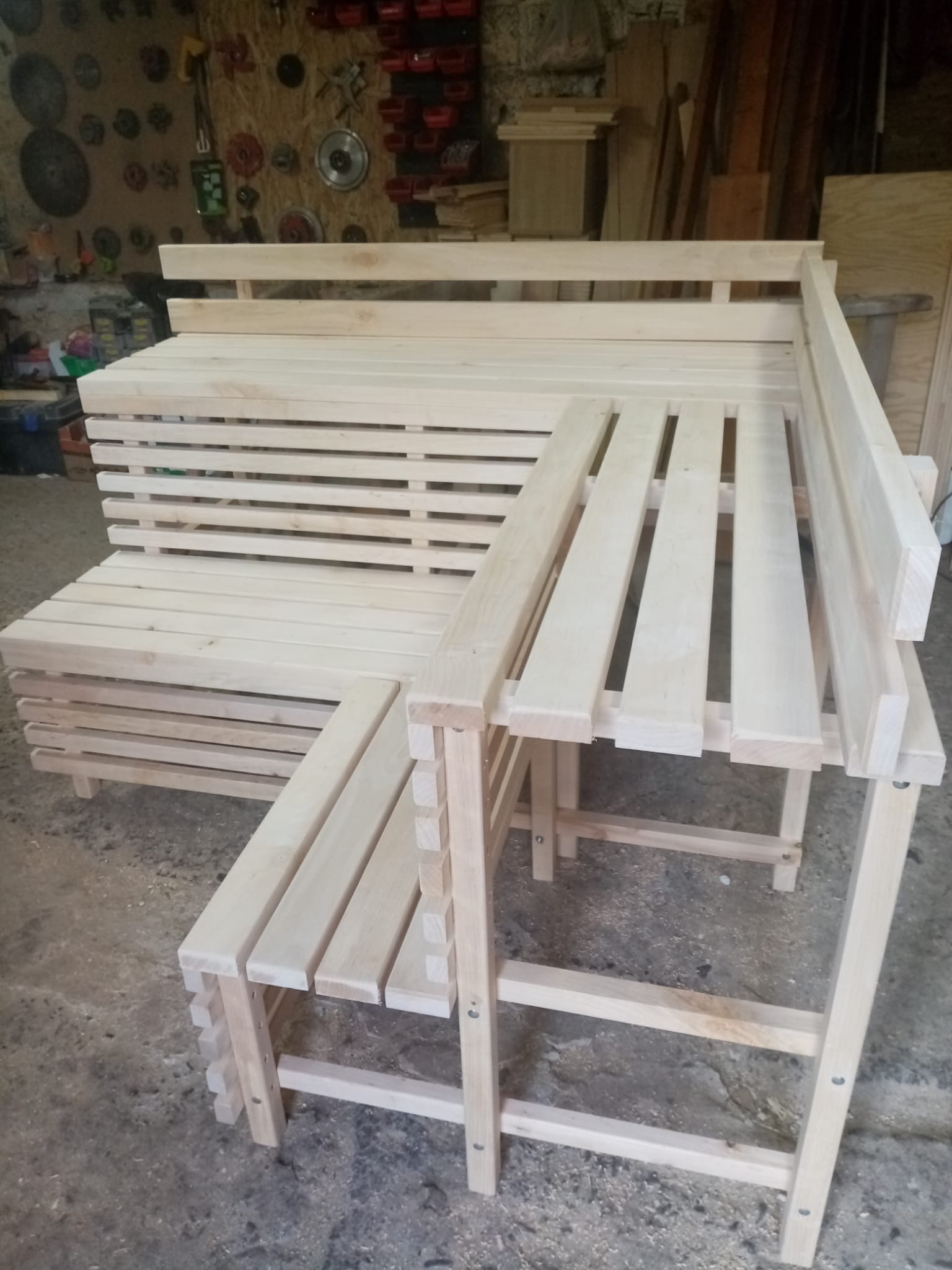 Surowy, drewniany narożnik z ławką i stolikiem, wykonany z jasnego drewna, widoczny w warsztacie z narzędziami na ścianie.