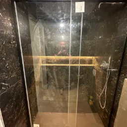 Kabina prysznicowa z przesuwnymi drzwiami, wykończona czarnym marmurem, z widocznym oświetleniem LED na półkach wewnątrz kabiny i naklejką informacyjną na szkle.