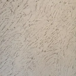 Tekstura ściany pokrytej szarą, dekoracyjną masą z wyraźnymi, nieregularnymi wzorami przypominającymi pociągnięcia pędzlem.