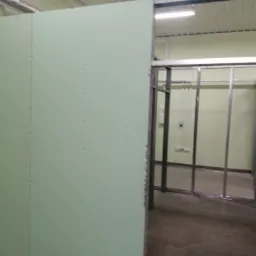 Wnętrze biura w trakcie remontu: widoczna ściana z płyty karton gips, częściowo zamontowana, oraz metalowy szkielet konstrukcyjny ścian działowych. Ściany pomalowane na jasnozielony kolor, widoczne...