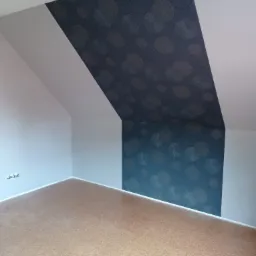 Poddasze po remoncie: pomalowane ściany na biało, fragment ściany z tapetą w odcieniach granatu z motywem geometrycznym, jasna podłoga korkowa.