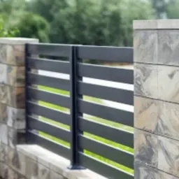 Nowoczesne ogrodzenie panelowe z szarymi, poziomymi przęsłami i słupkami wykończonymi dekoracyjną okładziną imitującą kamień, otoczone zielenią.