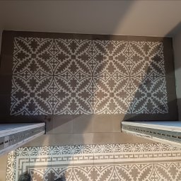 Glazur Usługi Budowlane Marcin Tokarz - Ułożona podłoga z płytek ceramicznych w łazience, wzór geometryczny w odcieniach szarości i bieli, widoczne fragmenty progów drzwiowych i butów