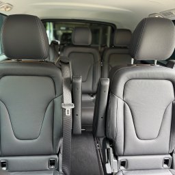 MBVBUS - Wnętrze luksusowego busa z czarnymi skórzanymi fotelami, widok z tyłu na trzy rzędy siedzeń z pasami bezpieczeństwa i zagłówkami, wnętrze pojazdu zadbane i czyste.