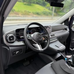 MBVBUS - Wnętrze luksusowego samochodu Mercedes-Benz: deska rozdzielcza z drewnianymi akcentami, skórzana tapicerka, kierownica z logo marki. Widok z perspektywy kierowcy.