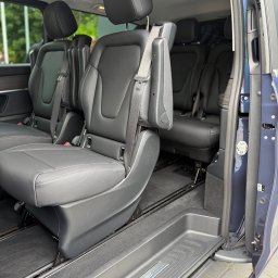 MBVBUS - Wnętrze komfortowego busa Mercedes-Benz z czarnymi skórzanymi fotelami, widok przez otwarte drzwi boczne. Widoczny system mocowania foteli.