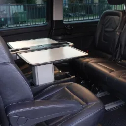 Luksusowe wnętrze busa z czarnymi skórzanymi fotelami, rozkładanymi stolikami i uchwytami na napoje. Widok z perspektywy pasażera.