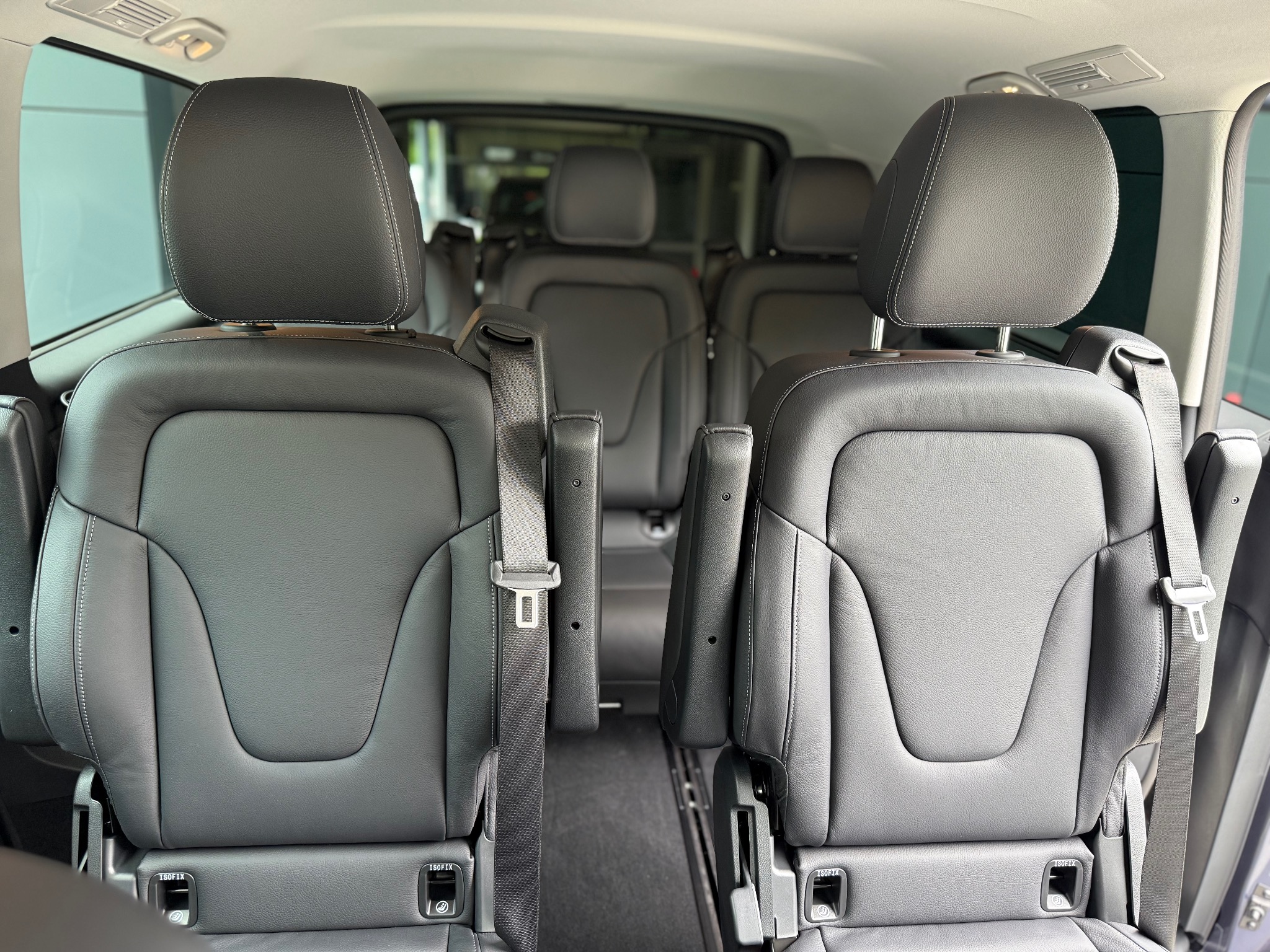 Wnętrze luksusowego busa z czarnymi skórzanymi fotelami, widok z tyłu na trzy rzędy siedzeń z pasami bezpieczeństwa i zagłówkami, wnętrze pojazdu zadbane i czyste.