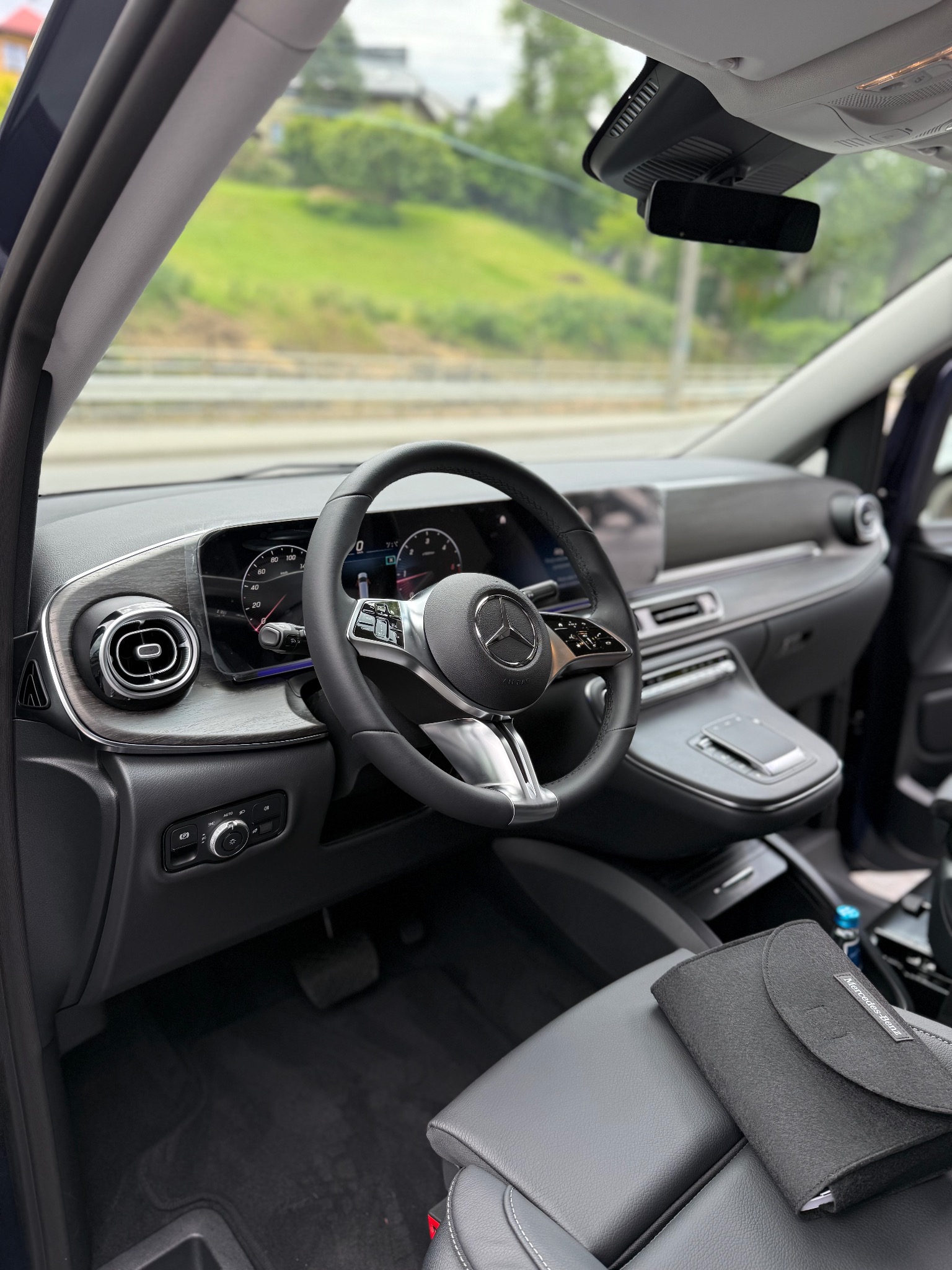 Wnętrze luksusowego samochodu Mercedes-Benz: deska rozdzielcza z drewnianymi akcentami, skórzana tapicerka, kierownica z logo marki. Widok z perspektywy kierowcy.