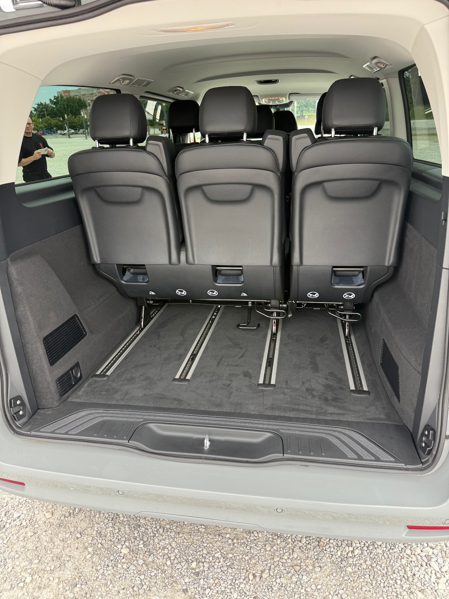 Wnętrze busa z widocznymi szynami do regulacji siedzeń, skierowane w stronę przedziału pasażerskiego. Widoczny fragment osoby w odbiciu szyby.