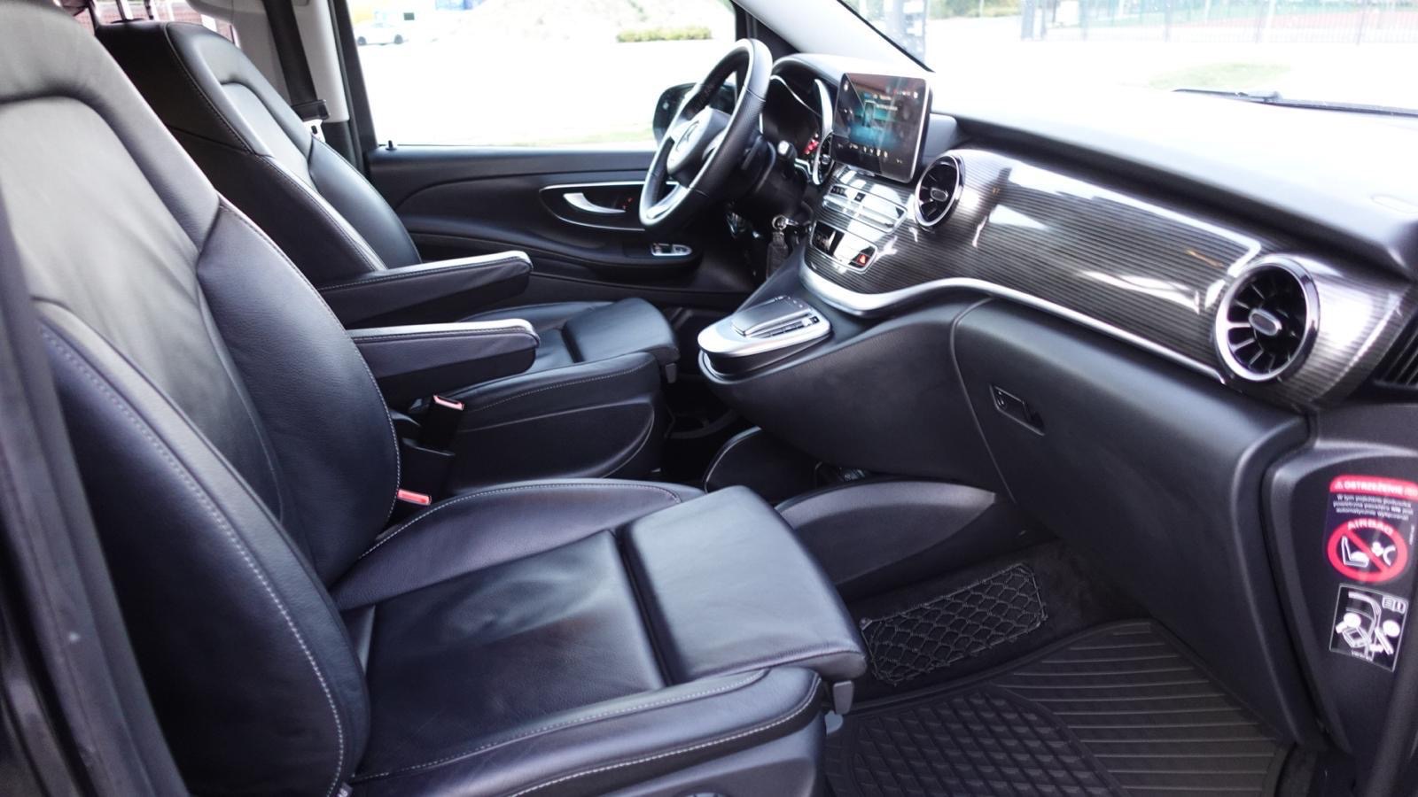 Wnętrze luksusowego busa z czarną skórzaną tapicerką, widoczne fotele z podłokietnikami, deska rozdzielcza z elementami karbonu i ekran dotykowy.
