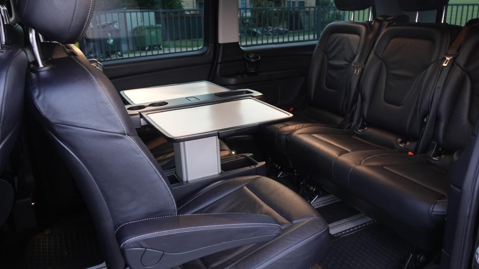 Luksusowe wnętrze busa z czarnymi skórzanymi fotelami, rozkładanymi stolikami i uchwytami na napoje. Widok z perspektywy pasażera.