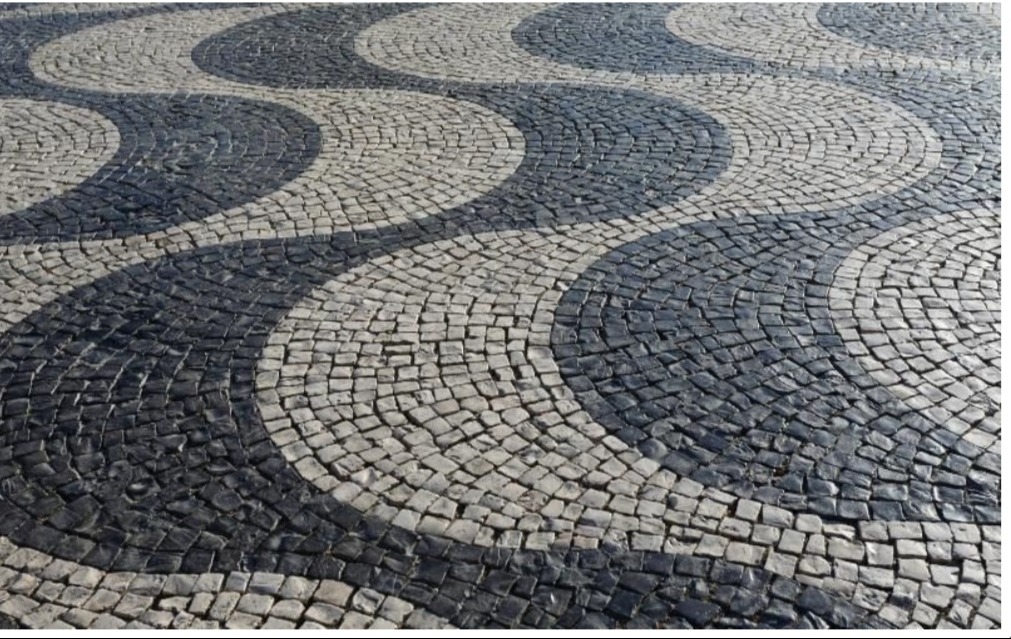 Czarno-biała kostka brukowa ułożona we wzór fal, tworząca dekoracyjny chodnik.
