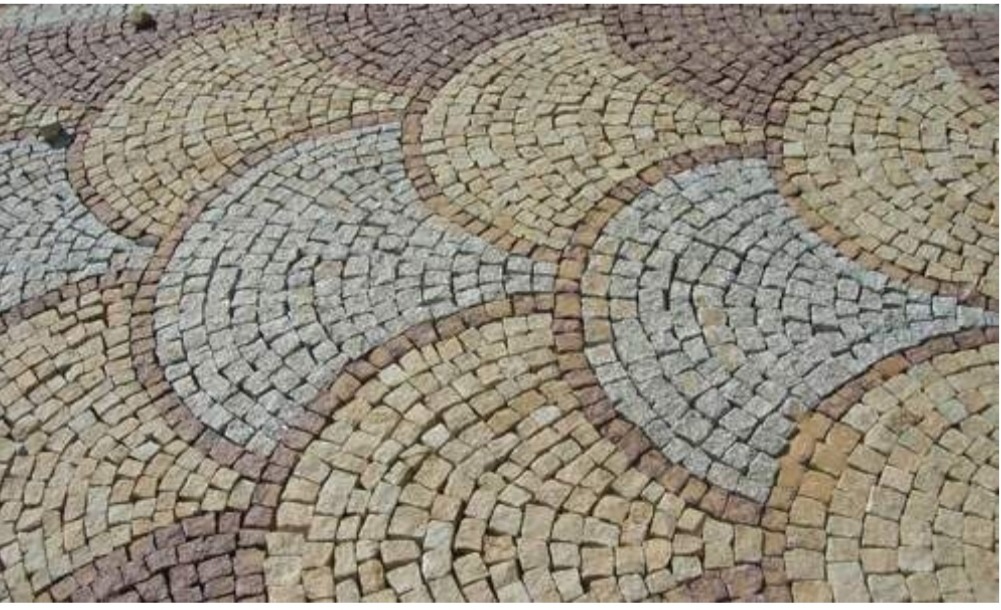 Dekoracyjna nawierzchnia z kostki granitowej ułożona w falujący wzór z wykorzystaniem odcieni szarości, beżu i brązu.